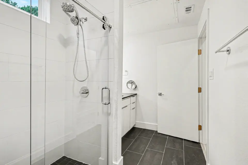 Glass-enclosed shower with a handheld showerhead and black tile flooring