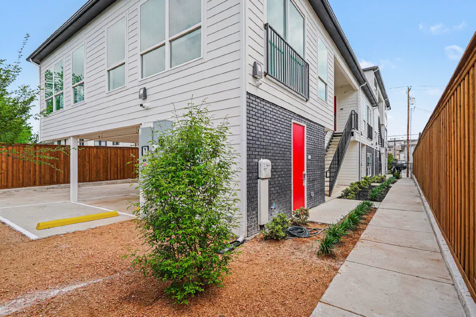Side exterior with covered parking, red entry doors, and landscaped walkway