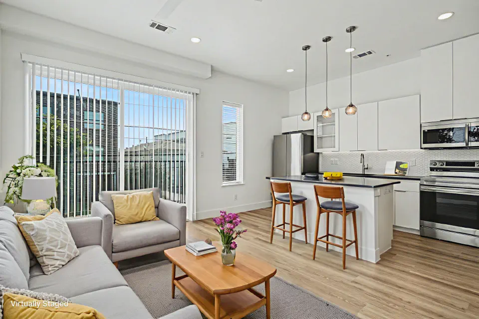 Living room and kitchen with island seating, pendant lights, and balcony access