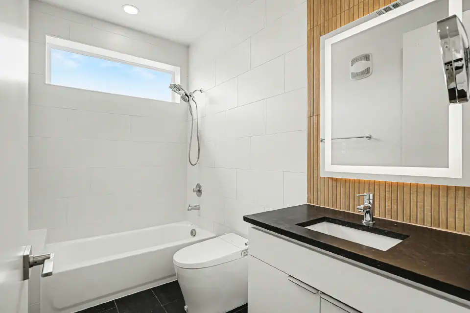 Bathroom with tub and shower, illuminated mirror, wood accent wall, and black countertop