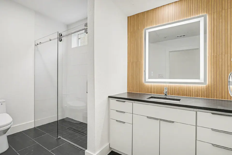 Bathroom with a glass-enclosed walk-in shower, wide vanity, and illuminated mirror